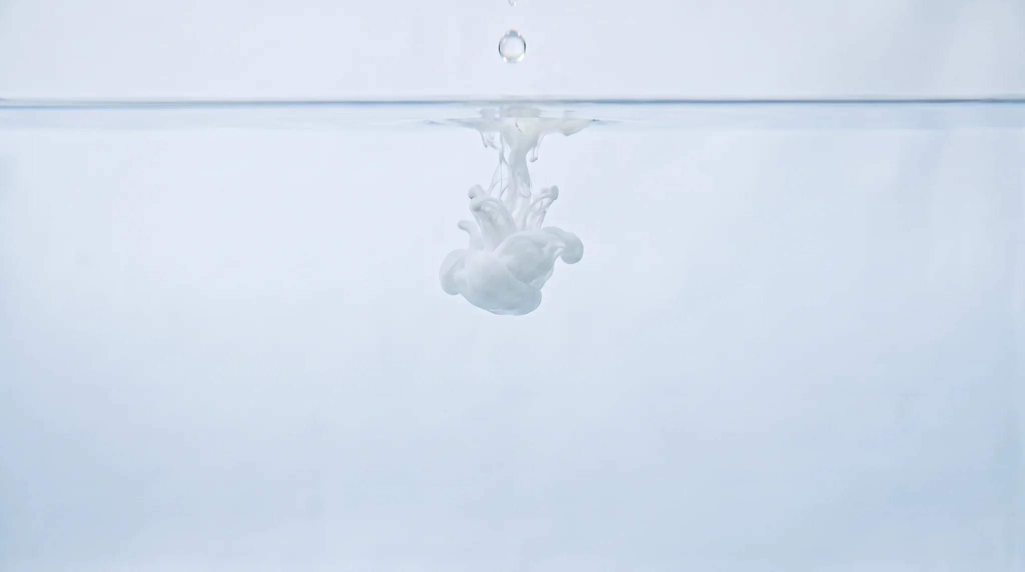 A drop of white ink dispersing through clear water